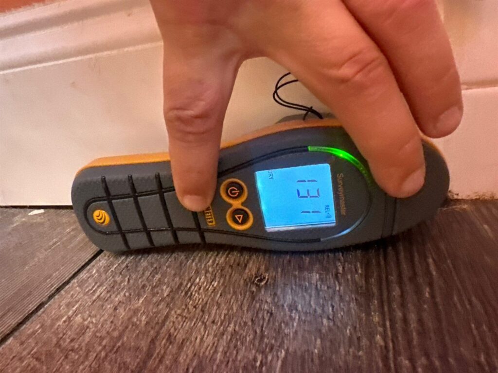 Moisture meter held against new plank flooring showing a reading in the dry range
