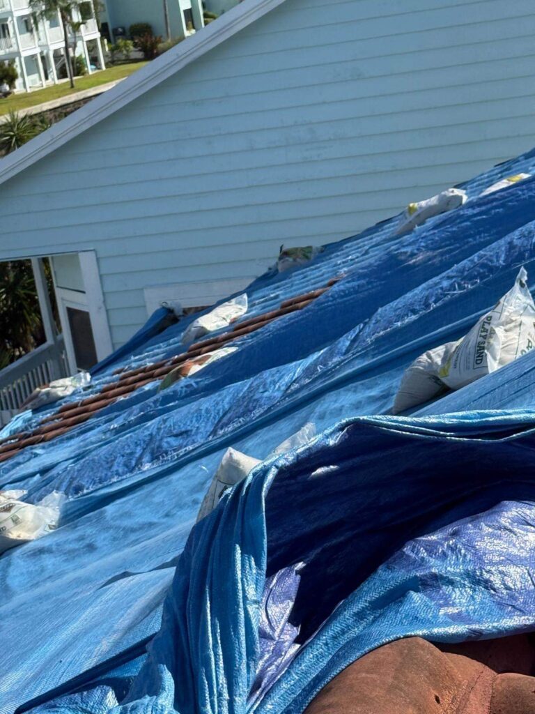 Blue emergency tarps and sandbags covering a storm damaged roof