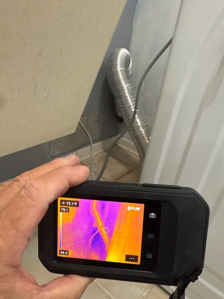 Technician holding a thermal imaging camera showing a heat map during a moisture inspection