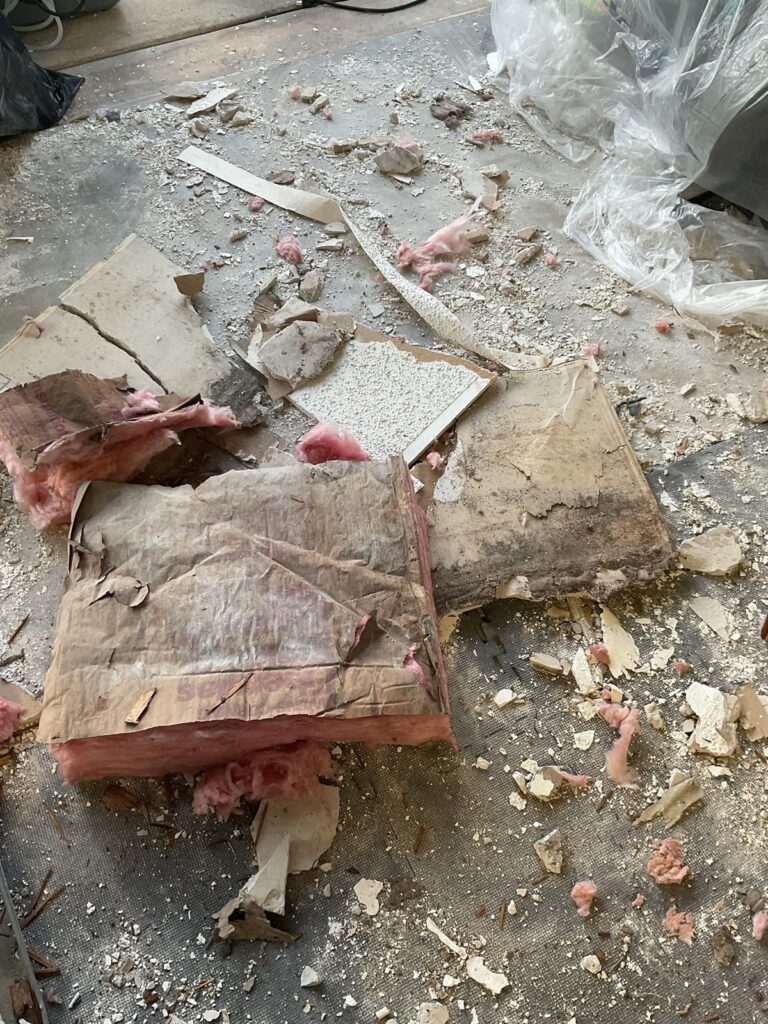 Fallen ceiling drywall and wet insulation piled on a protected floor after water damage
