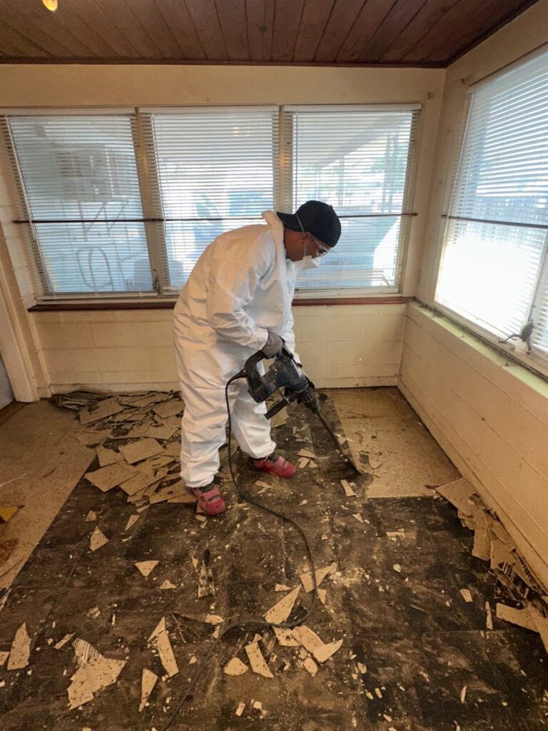 Restoration technician in protective gear removing damaged floor tile with a demolition hammer